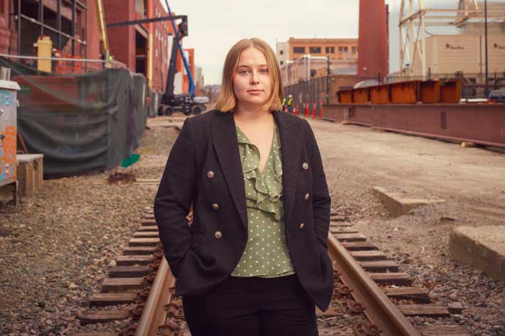 Mikayla Britsch stands on railway tracks near campus, with buildings in background